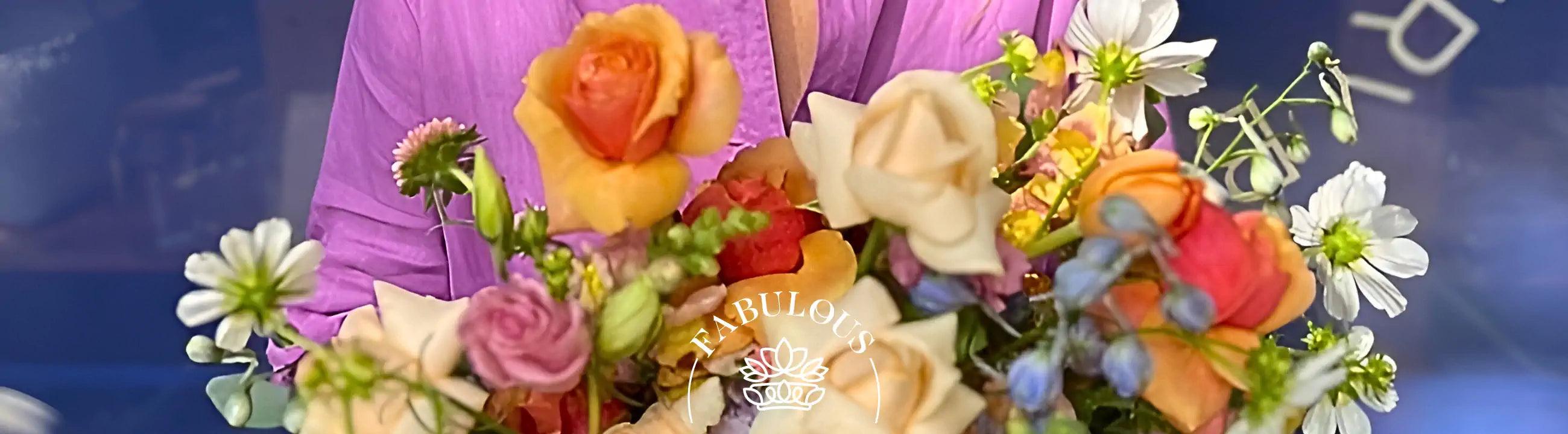 A close-up of a florist from Fabulous Flowers and Gifts in a pink blouse holding a vibrant bouquet of mixed flowers. Your Perfect Bouquet of Flowers.