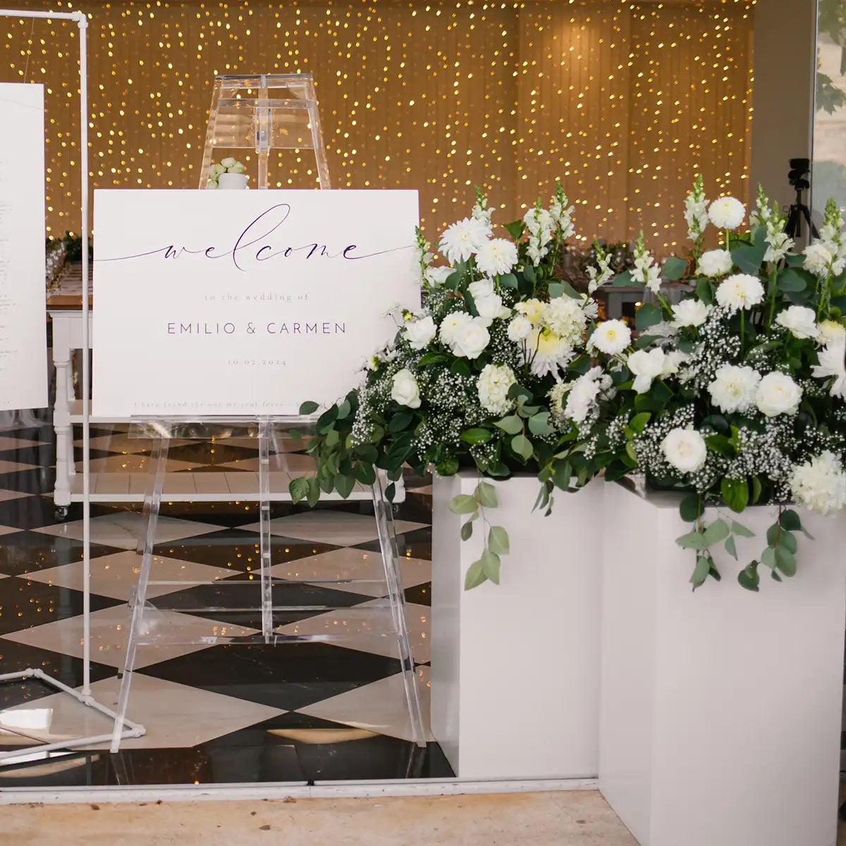Chic wedding welcome sign for Emilio & Carmen with elegant white floral arrangements and greenery in white planters. Ideal for event decor. Fabulous Flowers and Gifts."
