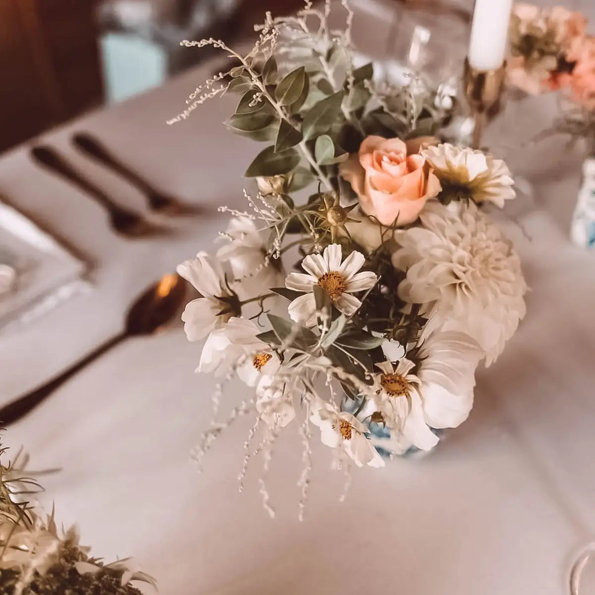 Close-up of an elegant table setting with a delicate floral arrangement featuring white daisies and peach roses. Perfect for events. Fabulous Flowers and Gifts.