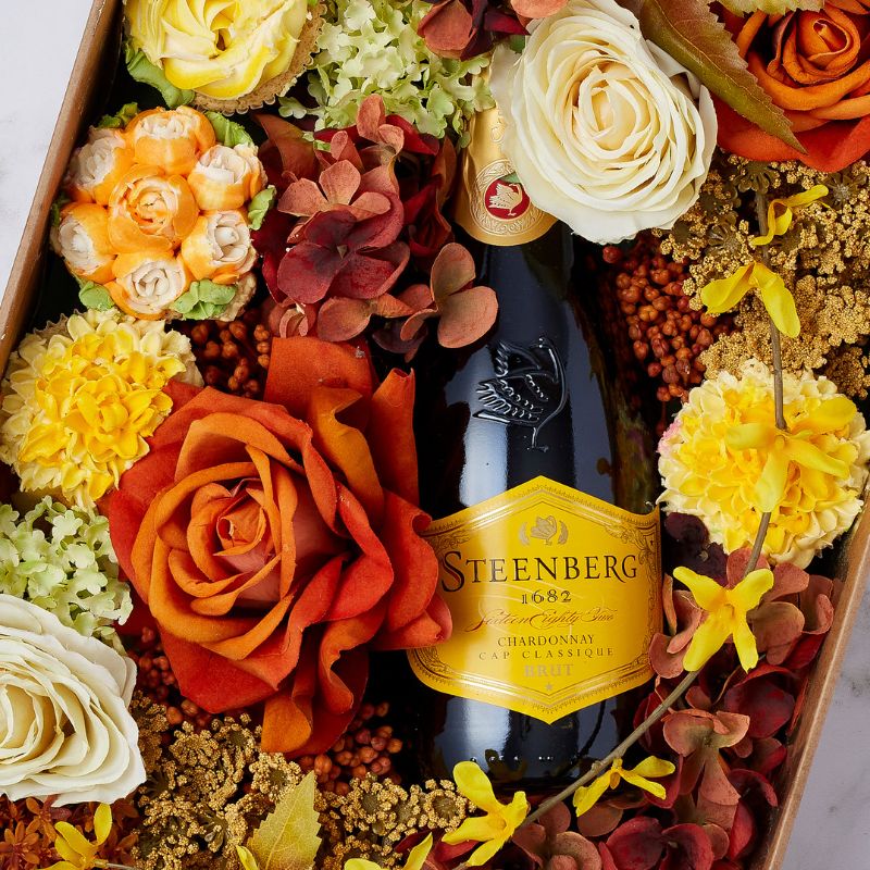 Close-up of Steenberg Chardonnay Brut bottle nestled in an arrangement of autumnal roses, hydrangeas, and seasonal blooms.