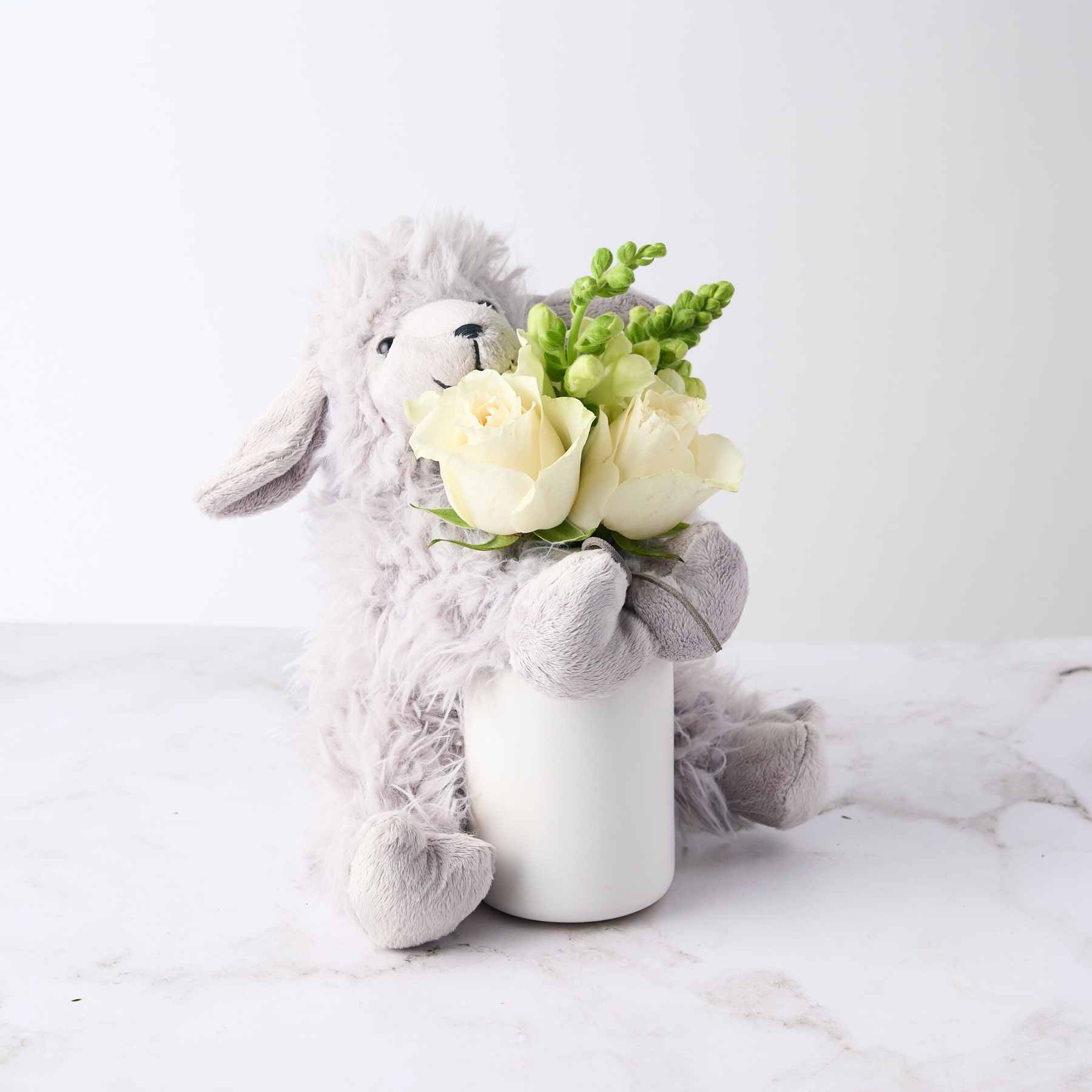 A soft grey plush toy holding a small vase with white roses and greenery, part of the 'Baby Boy Gift' arrangement.