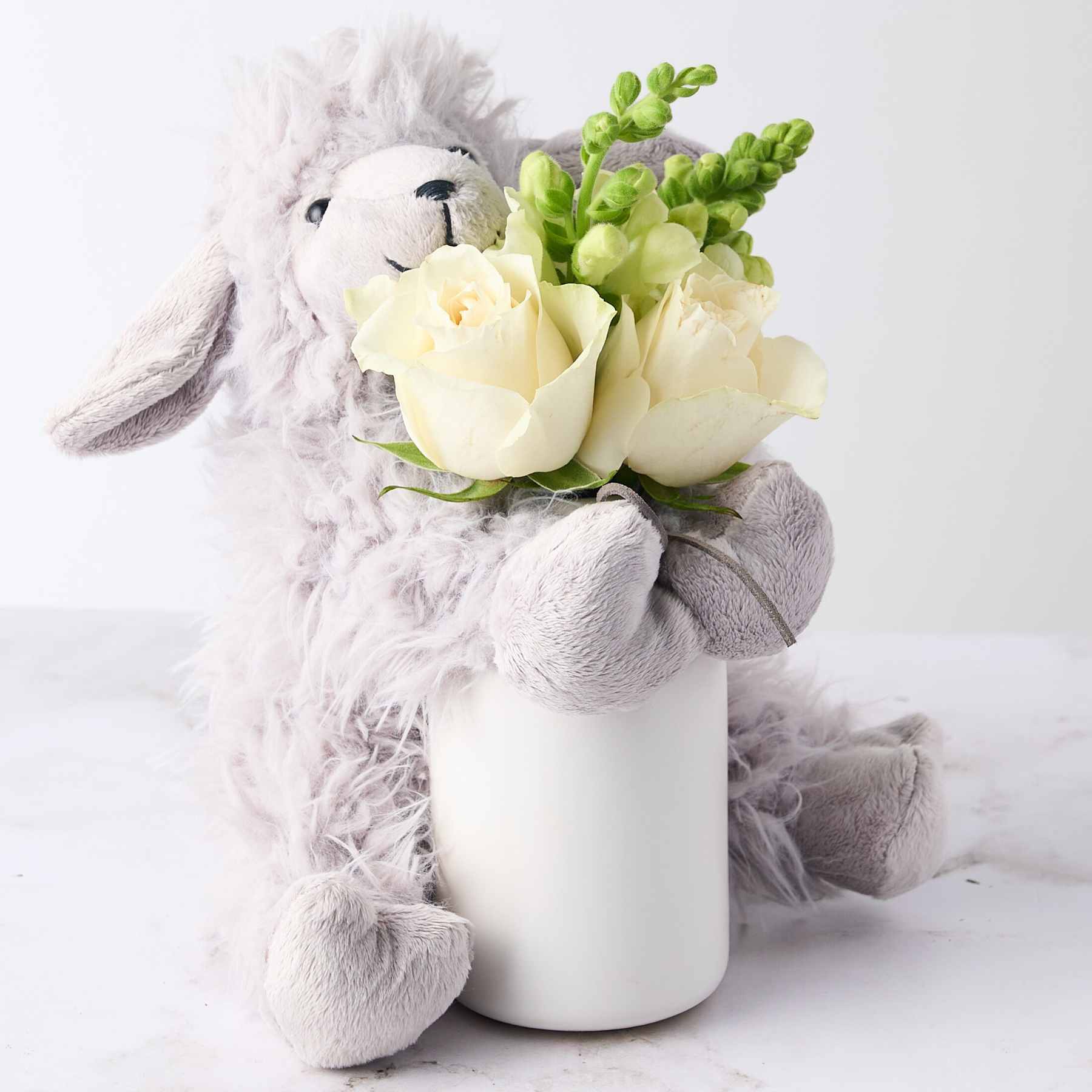 Close-up of a grey plush toy hugging a vase with white roses and green flowers, symbolising the 'Baby Boy Gift' arrangement.