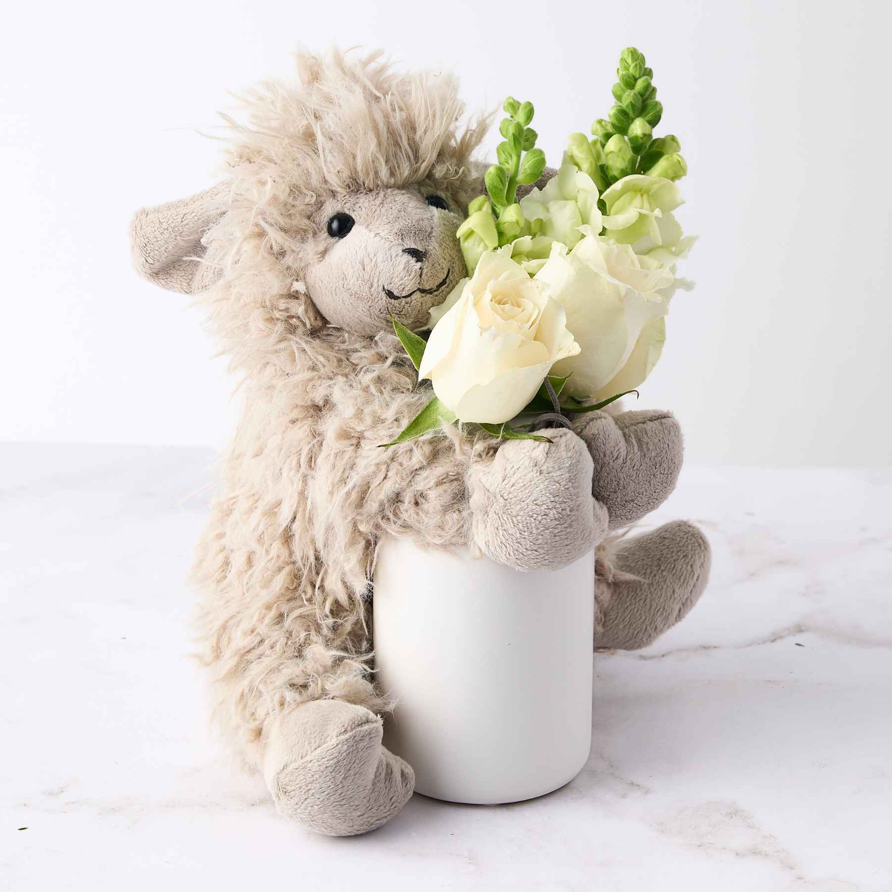 Close-up of a beige plush toy hugging a vase with white roses and green flowers, symbolising the 'Baby Girl Gift' arrangement.