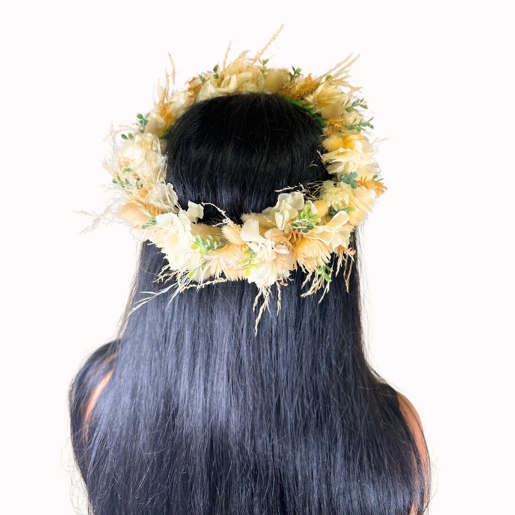 Back view of a woman with long black hair wearing a floral crown made with delicate yellow and cream flowers.