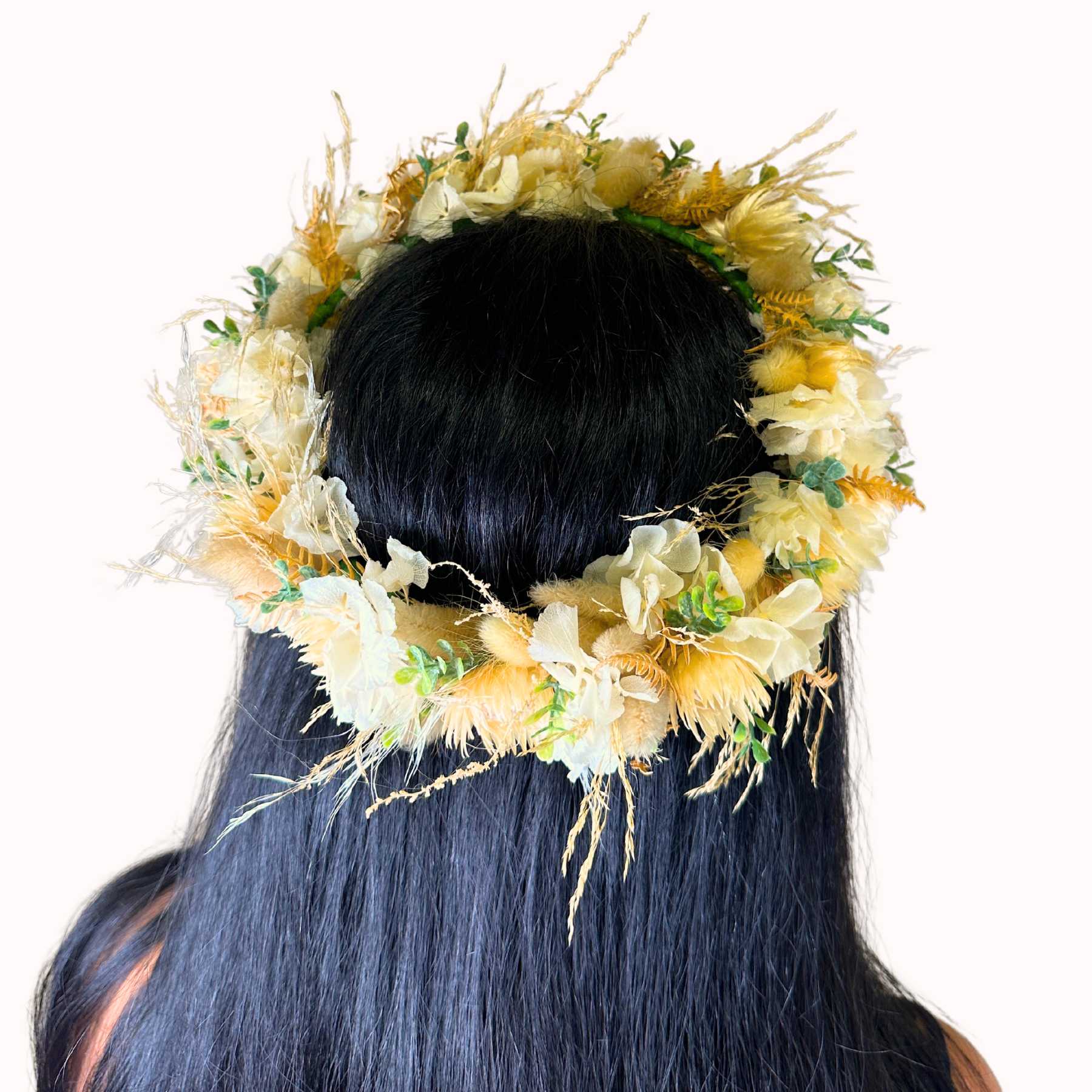 Zoomed in image of a  woman with long black hair adorned with a beautiful floral crown featuring yellow and cream flowers.