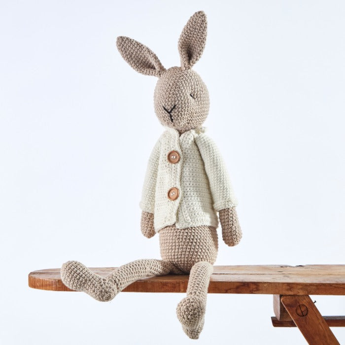 Benedict Bunny Gentleman, a handcrafted crochet bunny in a beige cardigan, sitting on a wooden bench