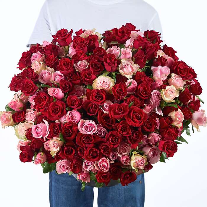 Close-up of 'Between Heartbeats' bouquet with lush red and pink roses, held by a happy man.