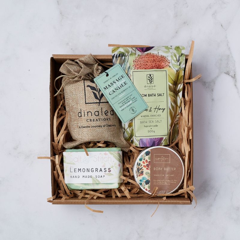 op view of the Blissful Indulgences gift box showcasing a selection of luxury self-care items, including a massage candle, bath salt, handmade soap, and body butter, packaged with shredded paper filler.