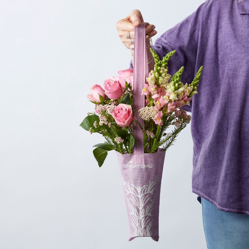 Person holding a purple floral tote bag filled with pink roses, snapdragons, and greenery