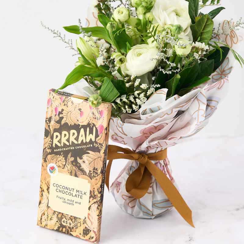 Bloom Boutique Posy - Close-up of a posy with white and green flowers wrapped in floral paper, paired with a Rrraw handcrafted coconut milk chocolate bar.