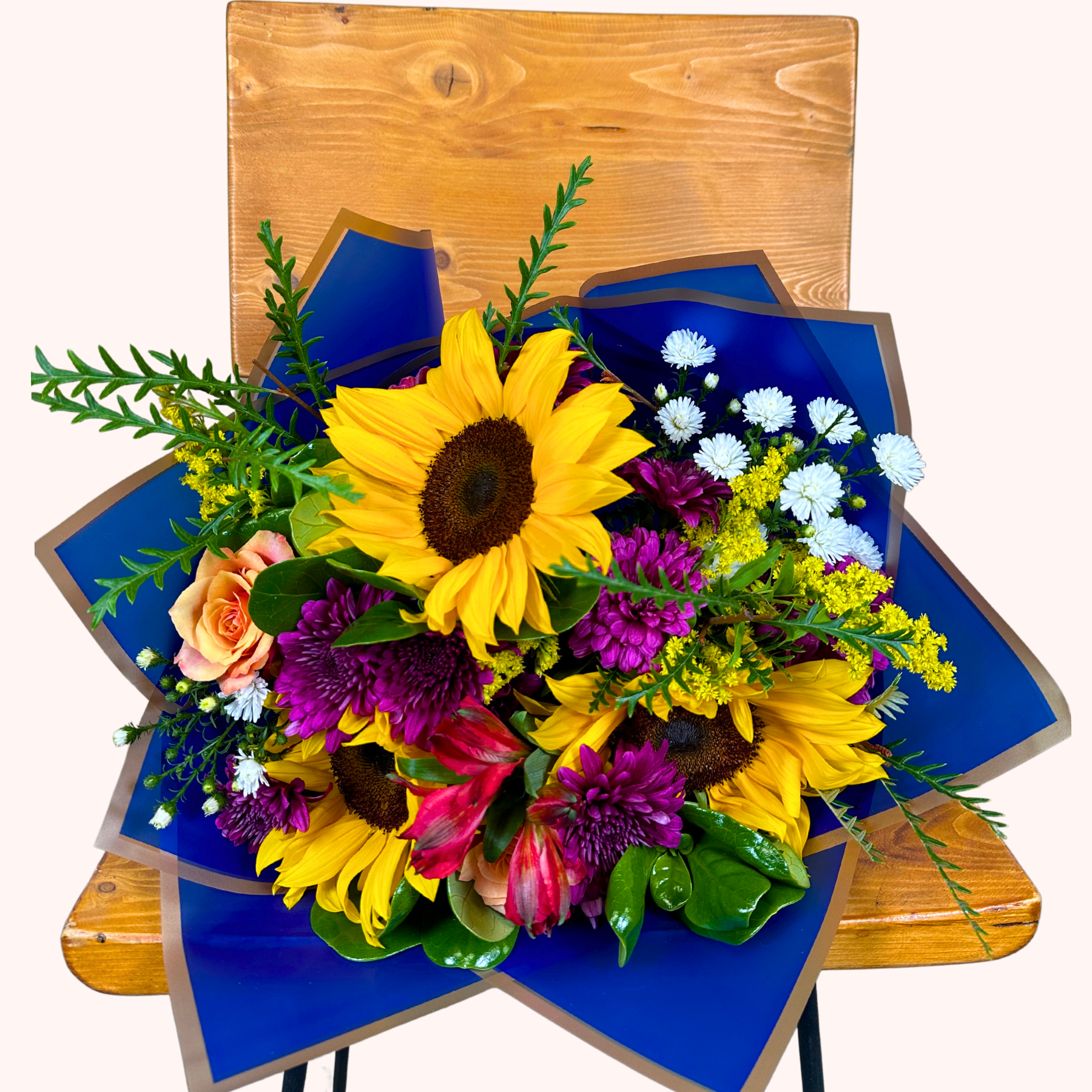 Blooming Sunshine Flower Bouquet with sunflowers, purple chrysanthemums, pink alstroemerias, orange roses, and white daisies, displayed on a wooden chair - Fabulous Flowers and Gifts