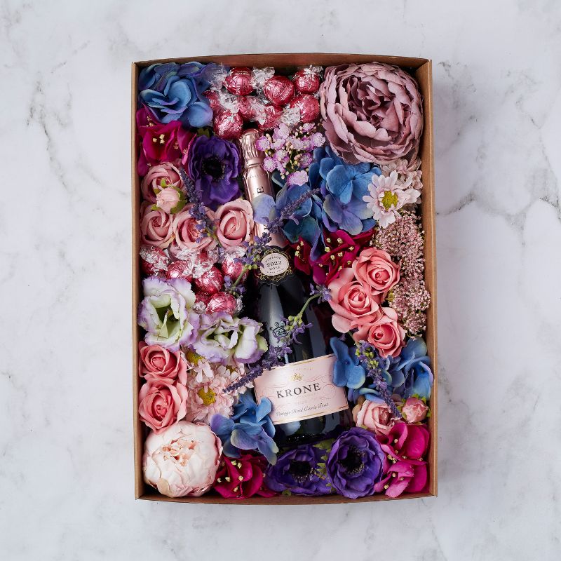 Luxury gift box with Krone Rosé sparkling wine surrounded by pink, purple, and blue flowers and Lindt chocolates