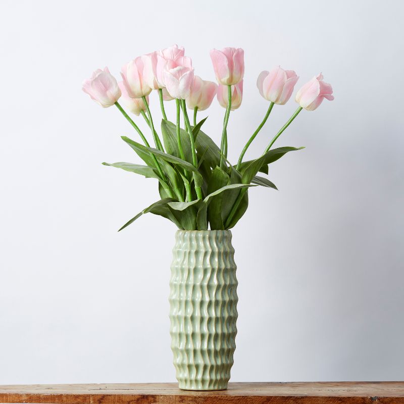 Artificial pink tulip arrangement in a textured green vase on a wooden surface, perfect for elegant home decor.