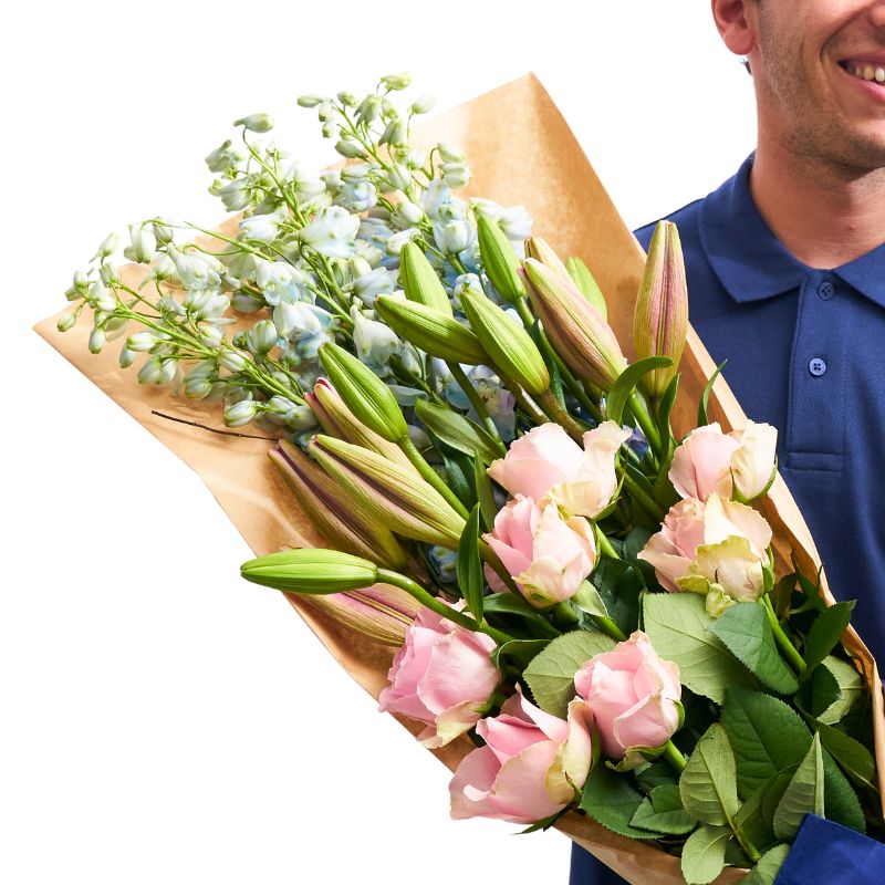 Elegant Blushing Beauty Bouquet with pink roses, fresh lilies, and soft blue delphiniums, hand-tied in luxury wrap from Fabulous Flowers.