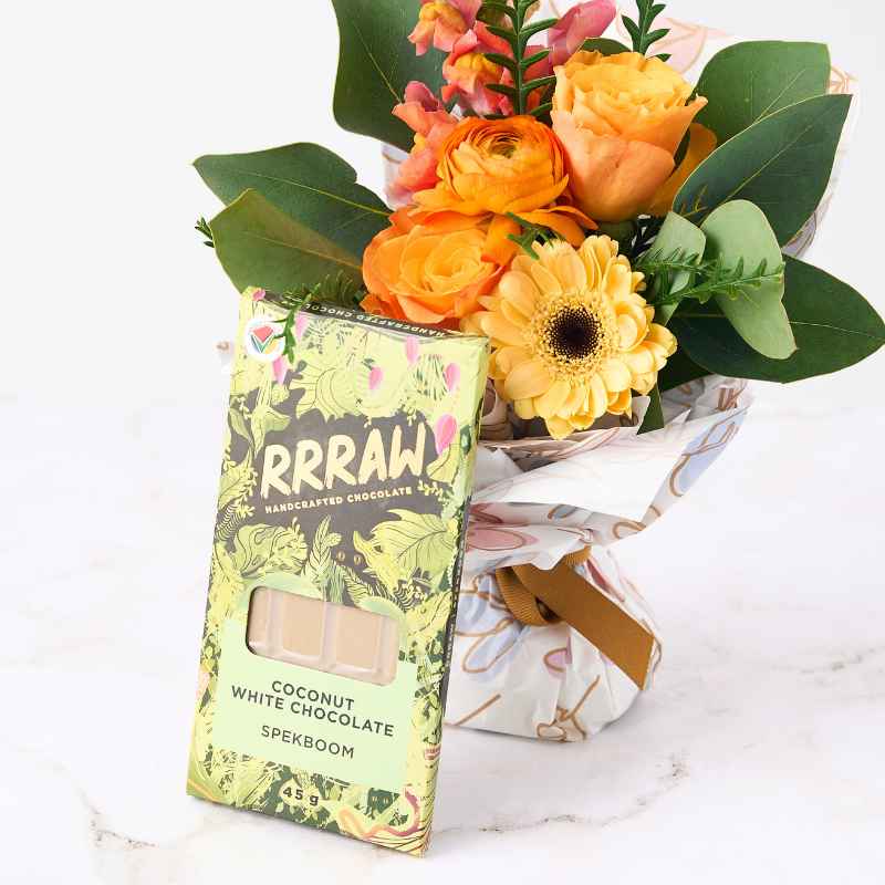 Botanical Beauty Posy - Close-up of a posy featuring bright orange and yellow flowers wrapped in floral paper, alongside a Rrraw handcrafted coconut white chocolate bar.