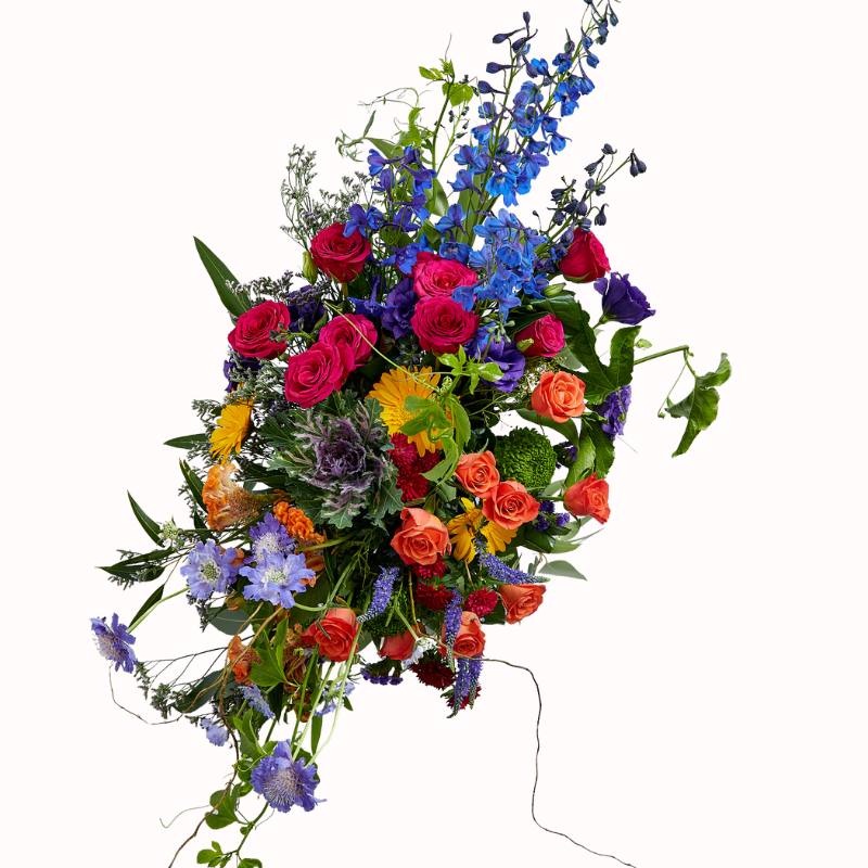 Tall, dramatic flower arrangement with roses, delphiniums, and cascading greenery on white.