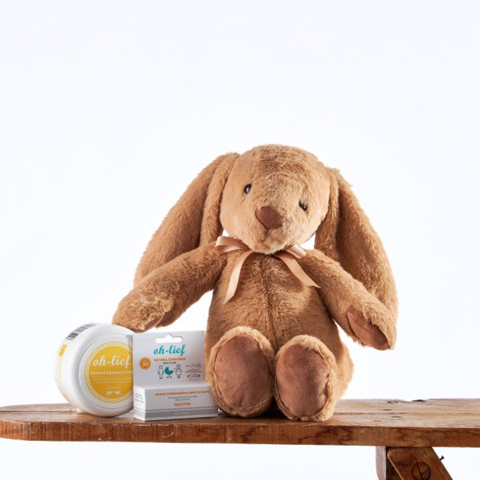 Bunny's Sun Safe Kit featuring a plush bunny toy alongside natural sunscreen and sunblock face stick on a wooden surface.