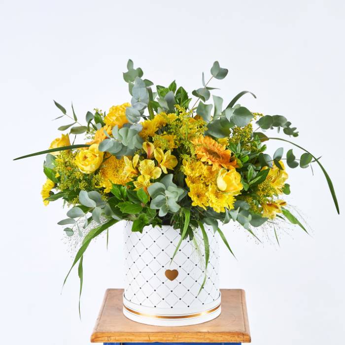 Buttercup Brilliance - A luxurious floral arrangement with vibrant yellow blooms, sunflowers, roses, and lush greenery in an elegant white box.