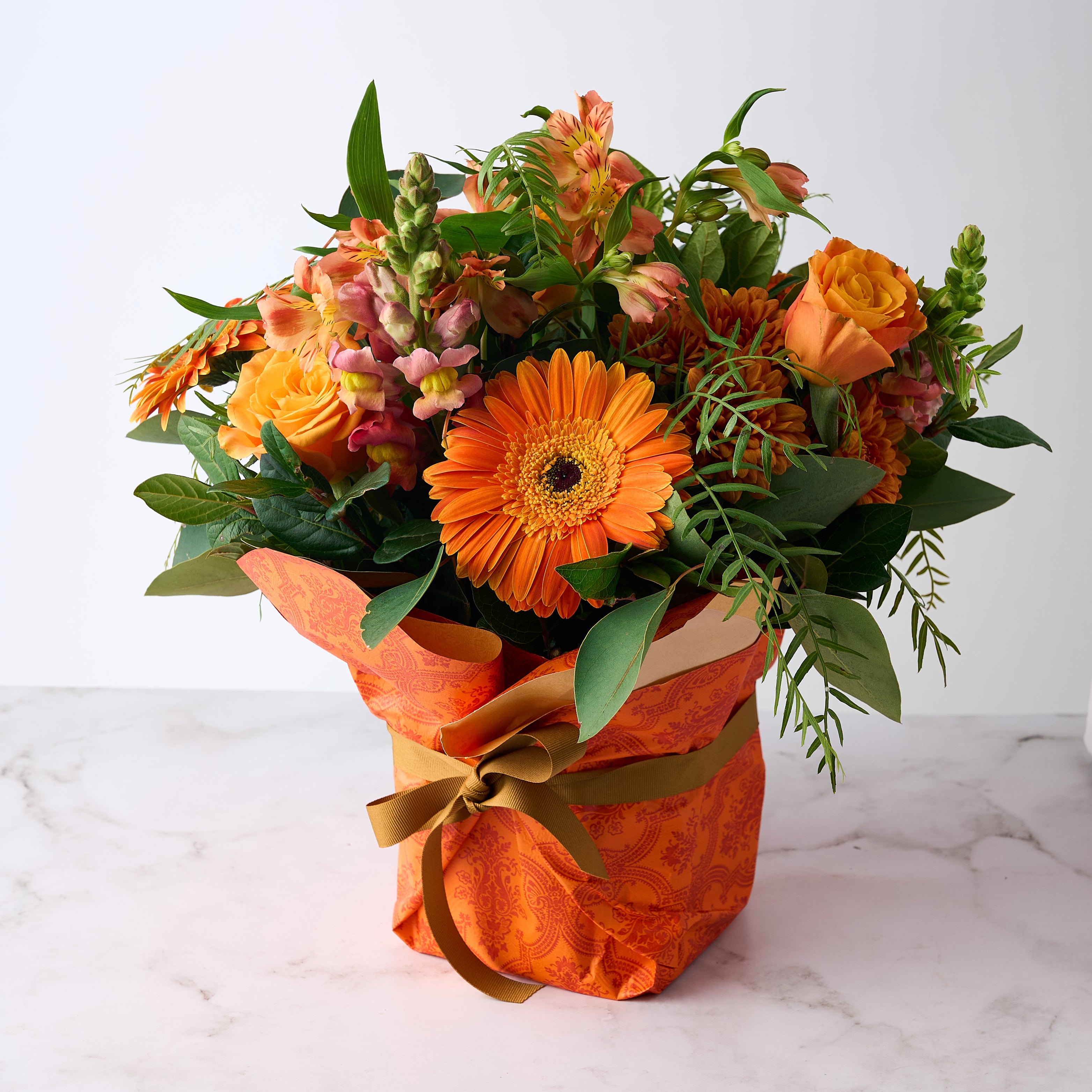 Celebrate Flower Arrangement featuring vibrant orange blooms wrapped in decorative paper with a bow.