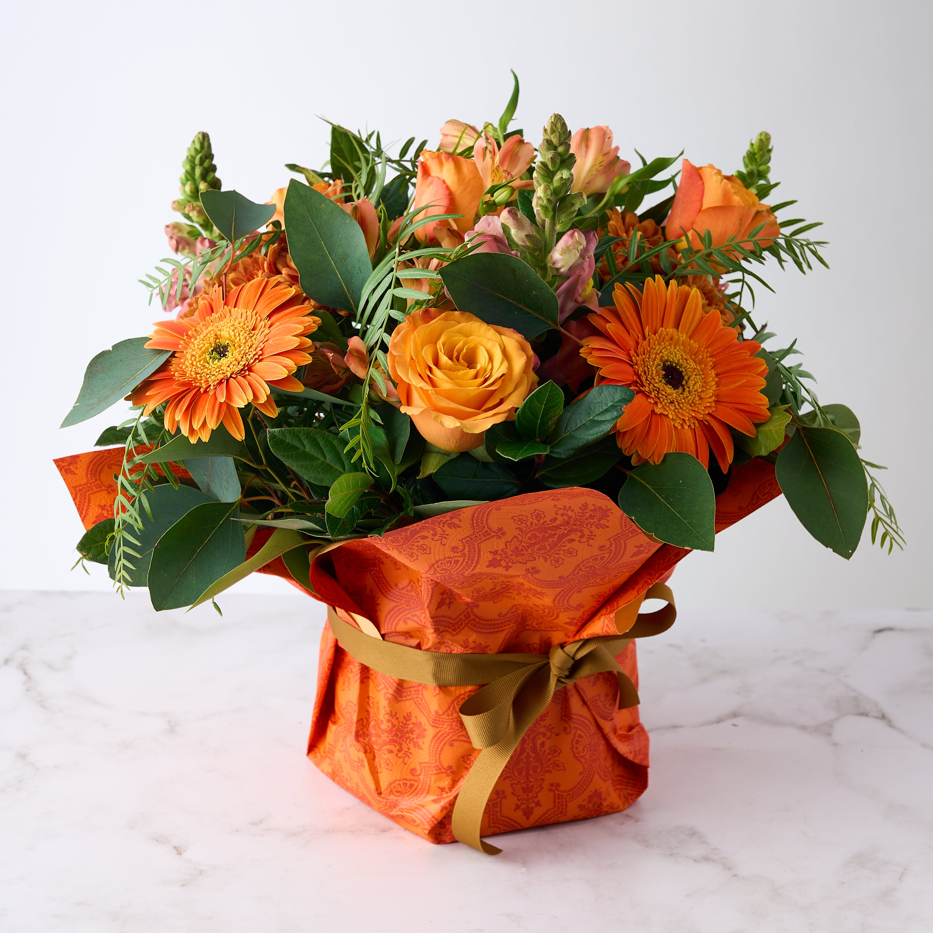 Bright Celebrate Flower Arrangement with orange flowers, elegantly wrapped in patterned paper with a ribbon.