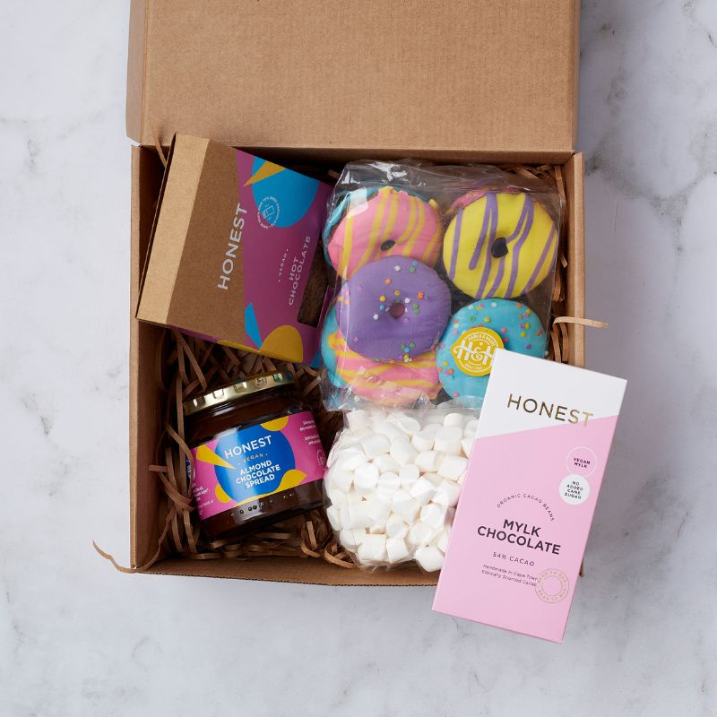 Vegan gift box with Honest Almond Chocolate Spread, colorful donuts, and Mylk Chocolate Bar arranged in a brown box.