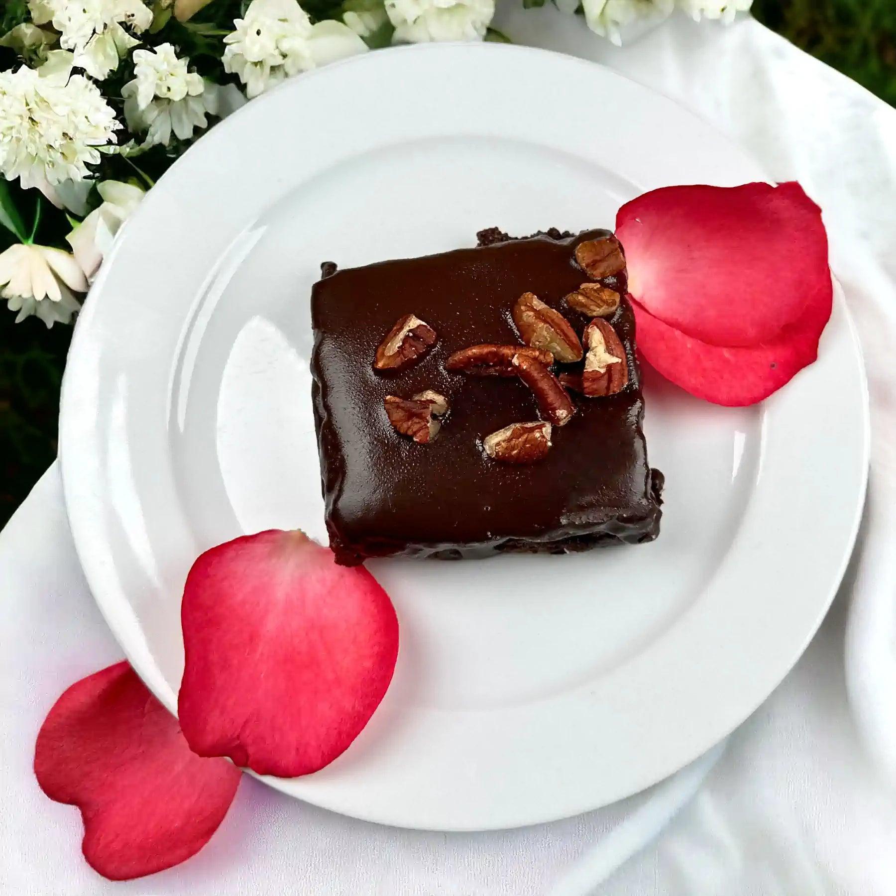 Decadent gluten-free chocolate brownie with pecans, garnished with red rose petals and white flowers. Fabulous Flowers and Gifts.