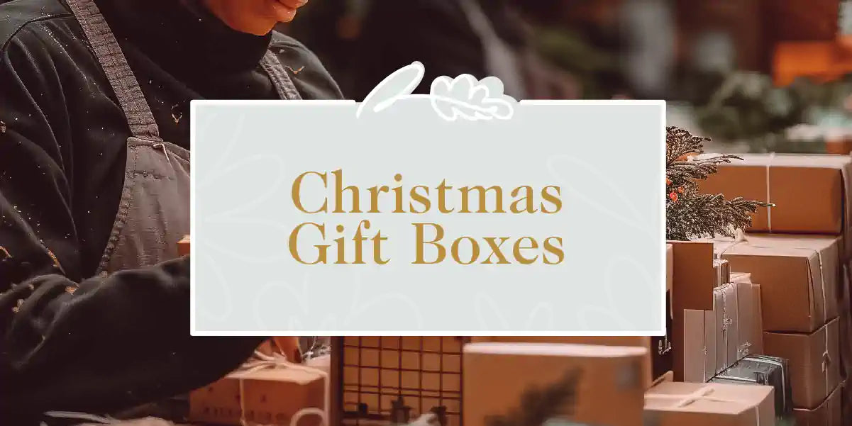 A person arranging festive Christmas gift boxes adorned with seasonal decorations. Fabulous Flowers and Gifts - Christmas Gift Boxes