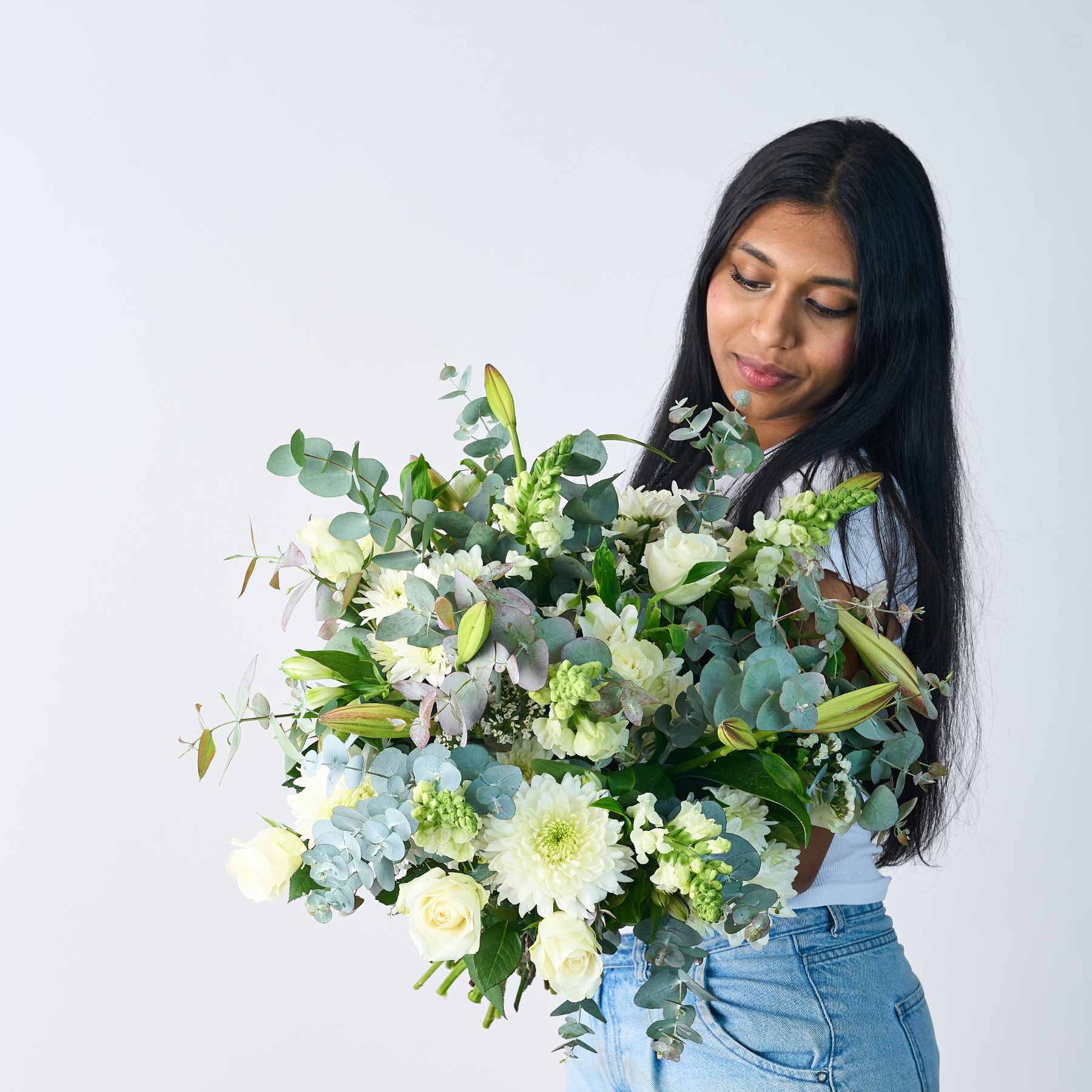 Woman holding a lush Classic White Bouquet, featuring a mix of white flowers and green foliage.