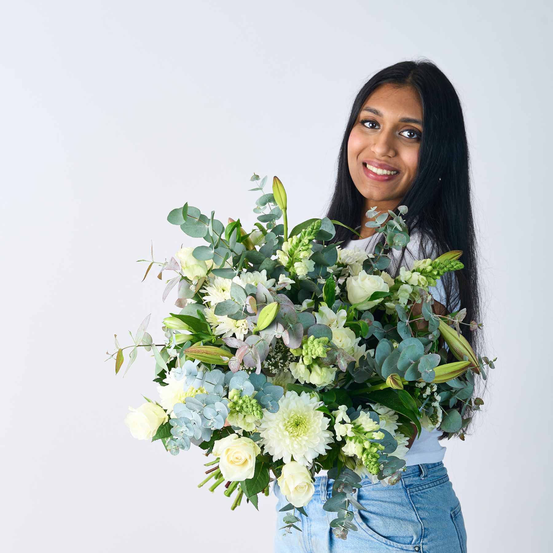 Smiling woman presenting a beautifully arranged Classic White Bouquet with white flowers and greenery.