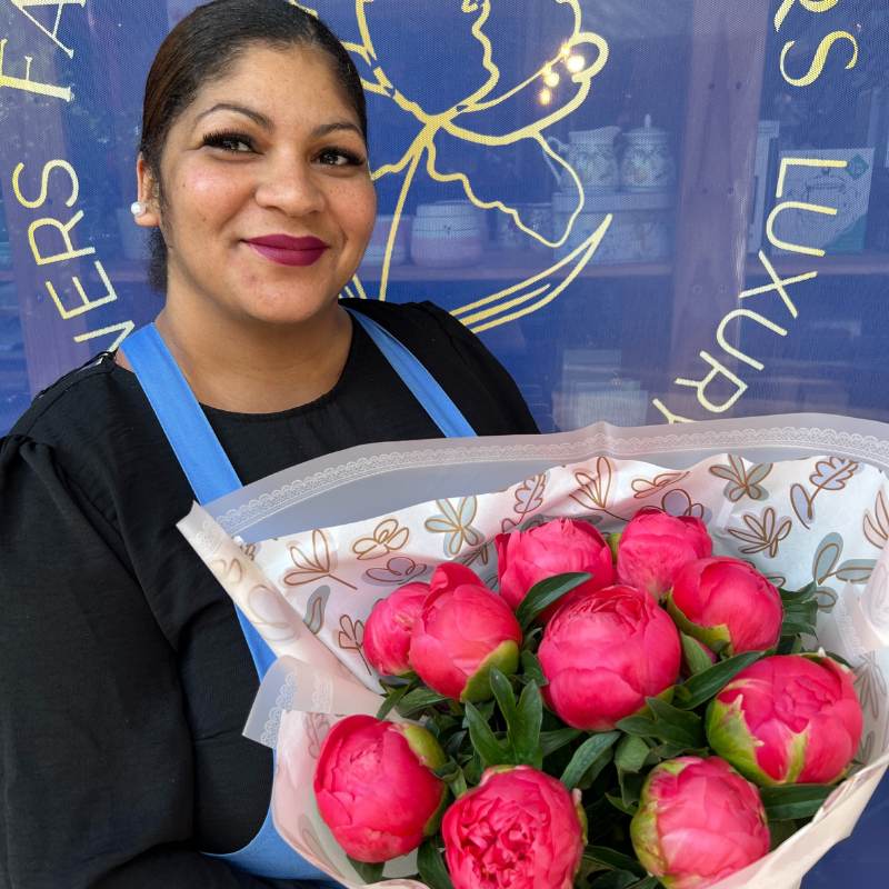 Smiling florist holding a vibrant Coral Sunset Peony bouquet with 10 stems wrapped in elegant paper - Fabulous Flowers & Gifts.