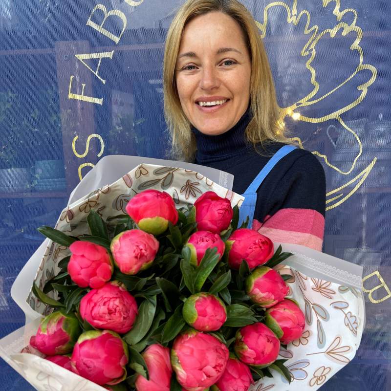 Florist holding a vibrant bouquet of 20 coral sunset peonies wrapped in elegant floral paper, available from Fabulous Flowers & Gifts.