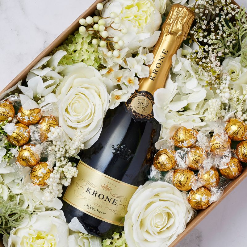 lose-up of Krone sparkling wine surrounded by white flowers and gold-wrapped Ferrero Rocher chocolates.