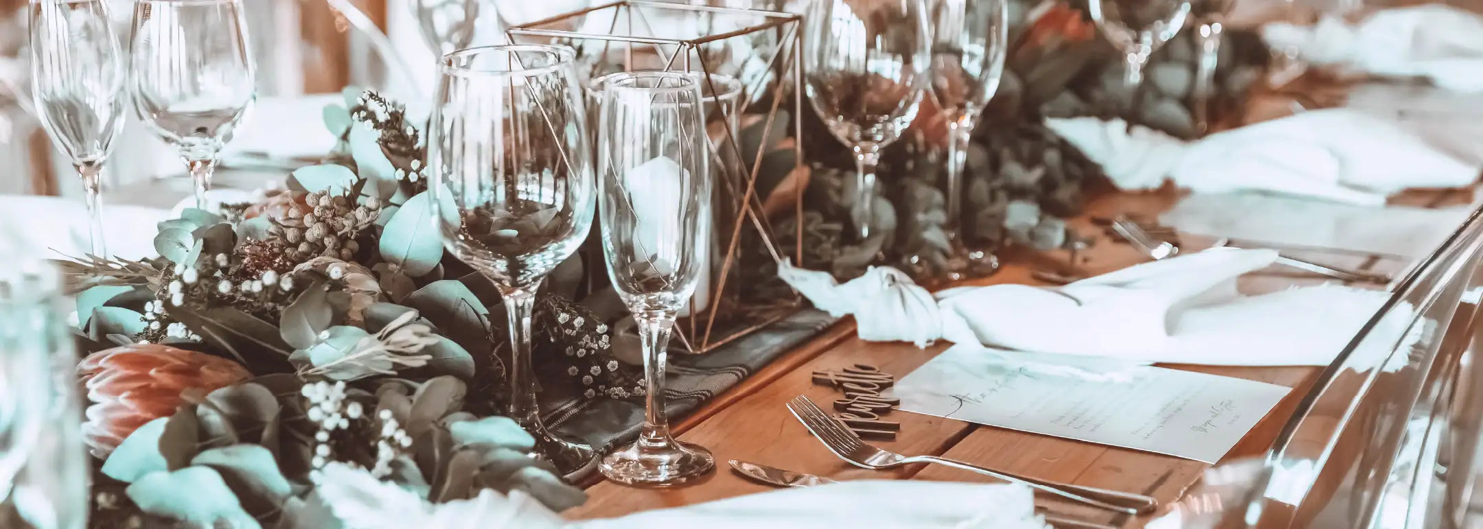 Close-up of a beautifully set event table with glassware, eucalyptus garlands, and candles, showcasing exquisite floral design. Chat to us today for memorable events. Fabulous Flowers and Gifts.