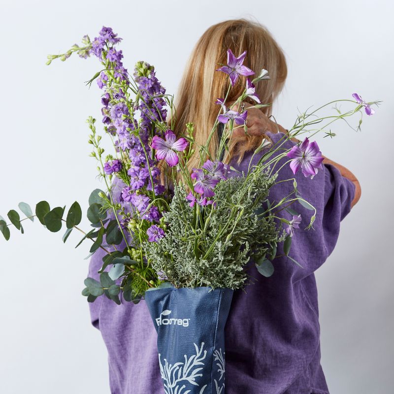 Woman holding a bouquet of fresh purple wildflowers and greenery in a reusable navy floral carrier bag.