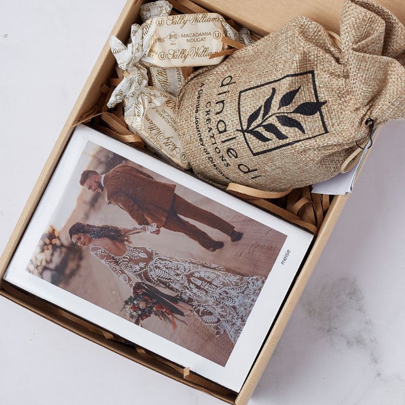 Welcome Home gift box featuring a framed wedding photo, Sally Williams nougat, and a Dinadi Creations burlap pouch.