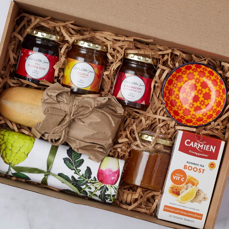 Close-up of Family Breakfast Gift Box showing jams, honey, bread roll, tea, colourful bowl, and napkin.