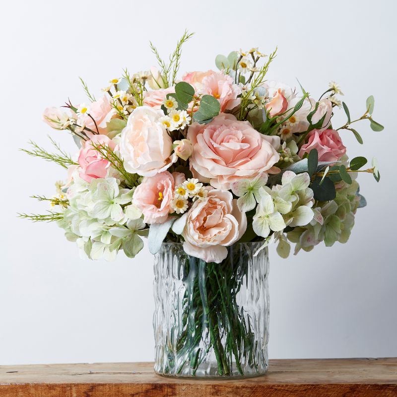 Forever Blush artificial flower arrangement displayed in a glass vase with realistic pink roses, peonies, white daisies, and eucalyptus.