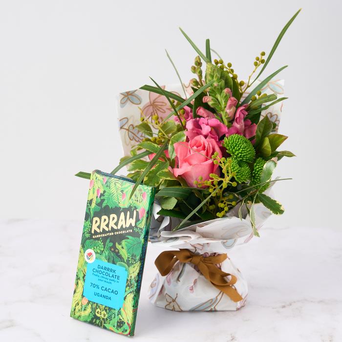 Chocolate & Blooms Gift Set featuring fresh seasonal flowers in pink and green hues, wrapped in decorative paper with a gold ribbon, paired with RRRAW 70% cacao dark chocolate.