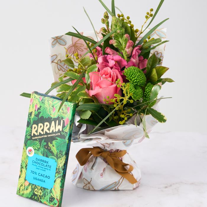 Chocolate & Blooms Gift Set featuring a vibrant posy of pink and green flowers, wrapped with a gold ribbon, alongside a RRRAW 70% cacao dark chocolate bar from Uganda.