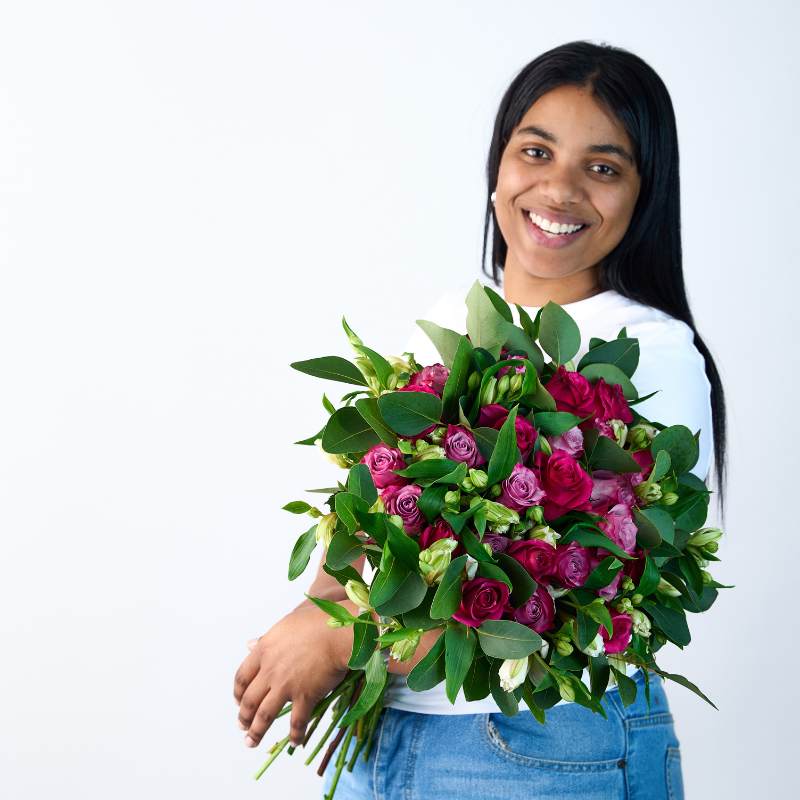 Smiling individual holding the Gentle Soul bouquet featuring vibrant pink and purple roses with lush green foliage - Fabulous Flowers & Gifts.