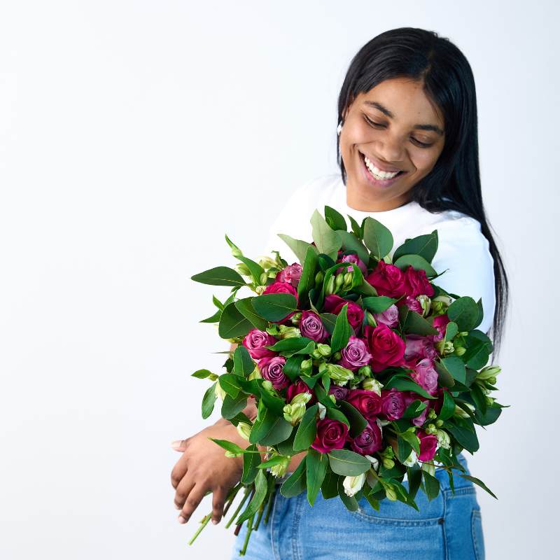 Joyful individual admiring the Gentle Soul bouquet with a stunning arrangement of pink and purple roses complemented by green foliage - Fabulous Flowers & Gifts.