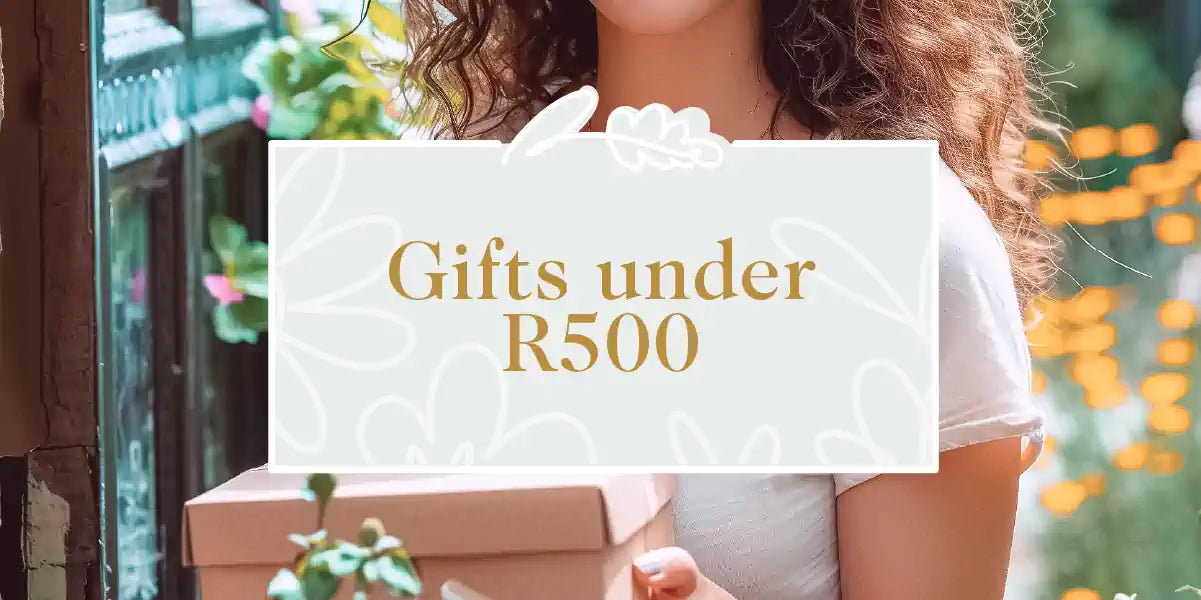A woman holding a budget-friendly gift box amidst a garden setting, showcasing affordability and beauty. Fabulous Flowers and Gifts - Gifts under R500