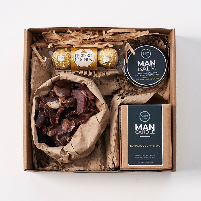 Close-up view of Gifts for a Man Hamper, featuring Ferrero Rocher chocolates, artisan-cured dried meat, and grooming products including a sandalwood and patchouli man balm and candle.