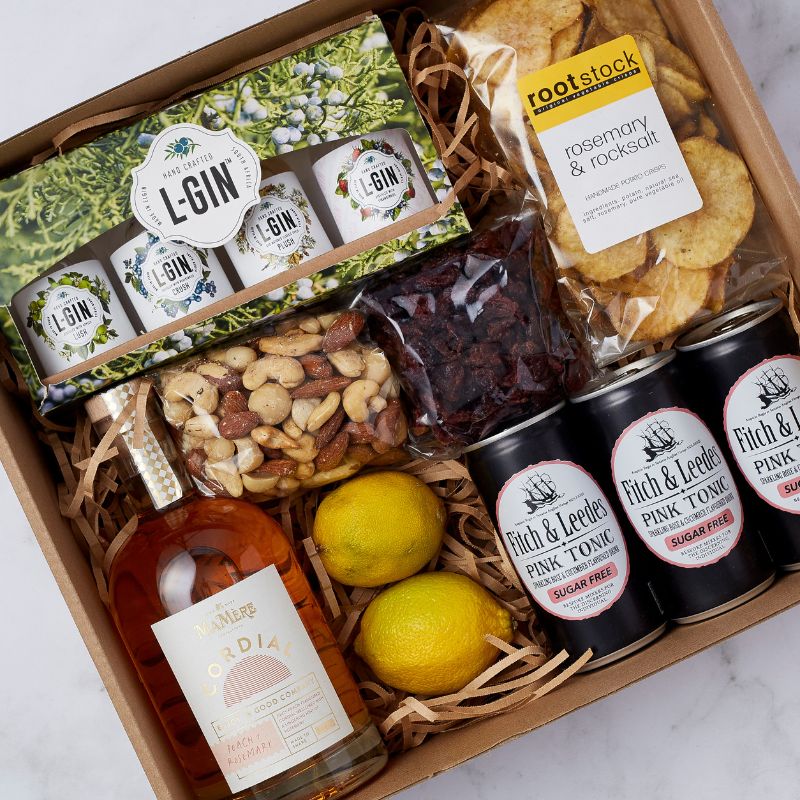 Top-down view of gin-themed gift box featuring L-GIN sampler, pink tonic, snacks, and fresh lemons.