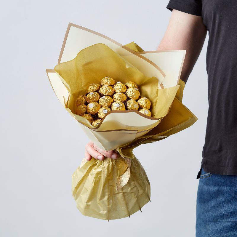 and holding a large Ferrero Rocher bouquet wrapped in golden paper, perfect for gifting.