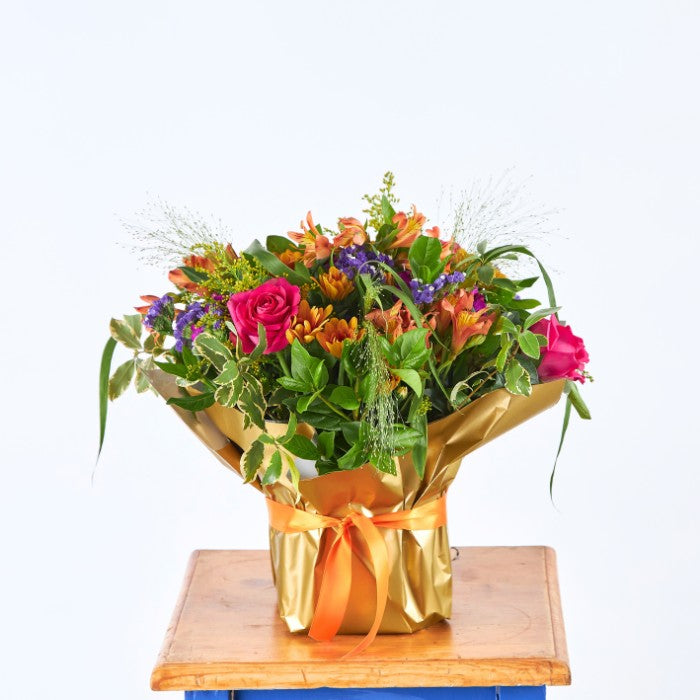 Grateful for You floral arrangement featuring bright roses, alstroemeria, and statice in a golden wrap, presented on a wooden table.