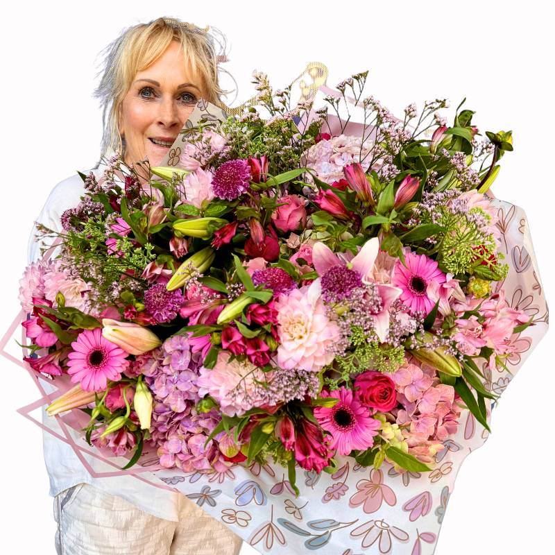 A stunning Handle with Love Bouquet featuring pink gerberas, roses, and lilies presented against a navy Fabulous Flowers Luxi backdrop by florist in white attire.