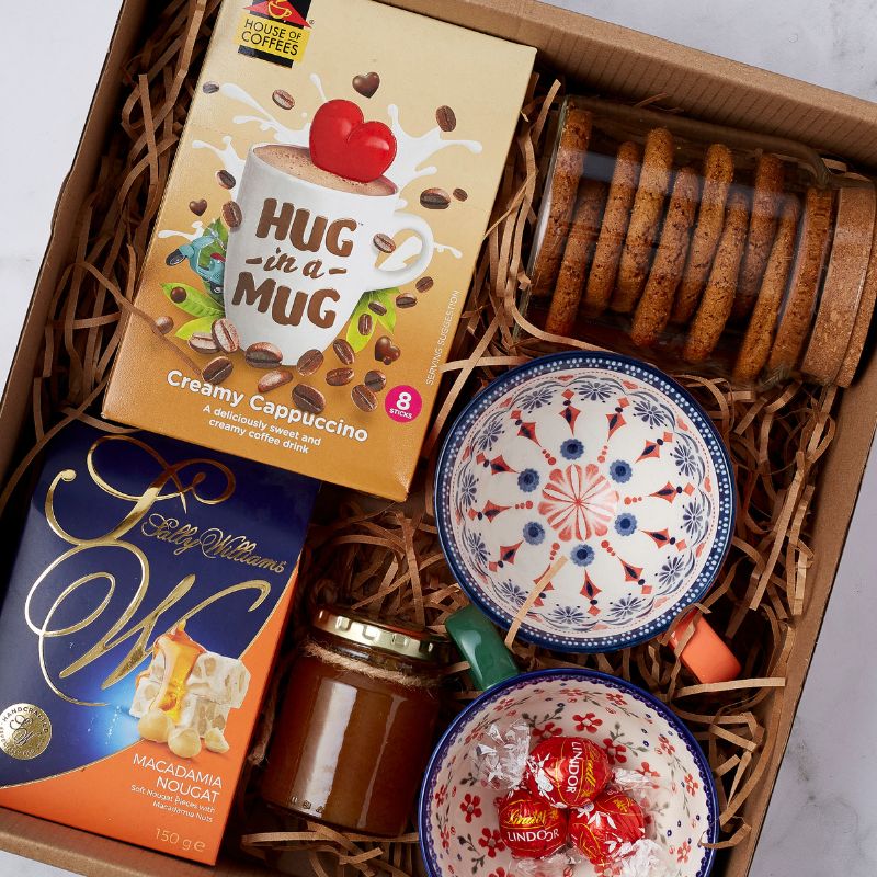 Close-up of gift box featuring Hug in a Mug cappuccino, nougat, honey jar, cookies, and colorful artisanal bowls