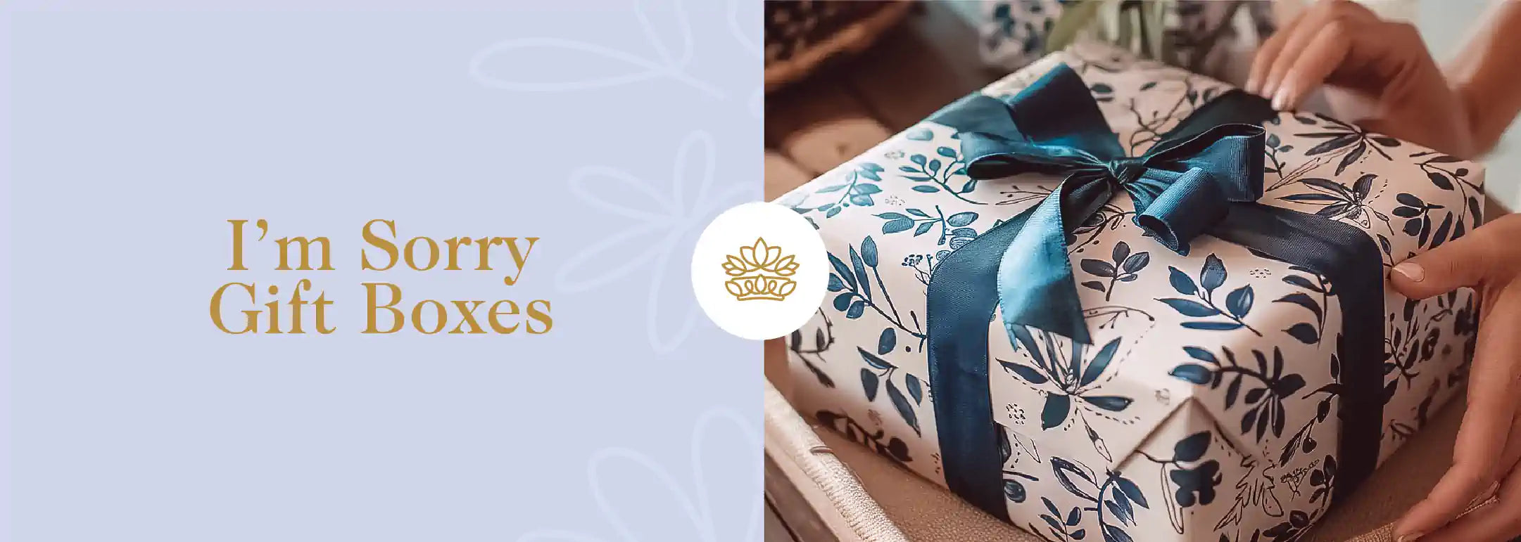 Hands delicately holding a beautifully wrapped gift box with a blue ribbon, adorned with floral patterns, symbolizing thoughtfulness and apology. Part of the I'm Sorry Gift Boxes Apology Gift Boxes Collection from Fabulous Flowers and Gifts.