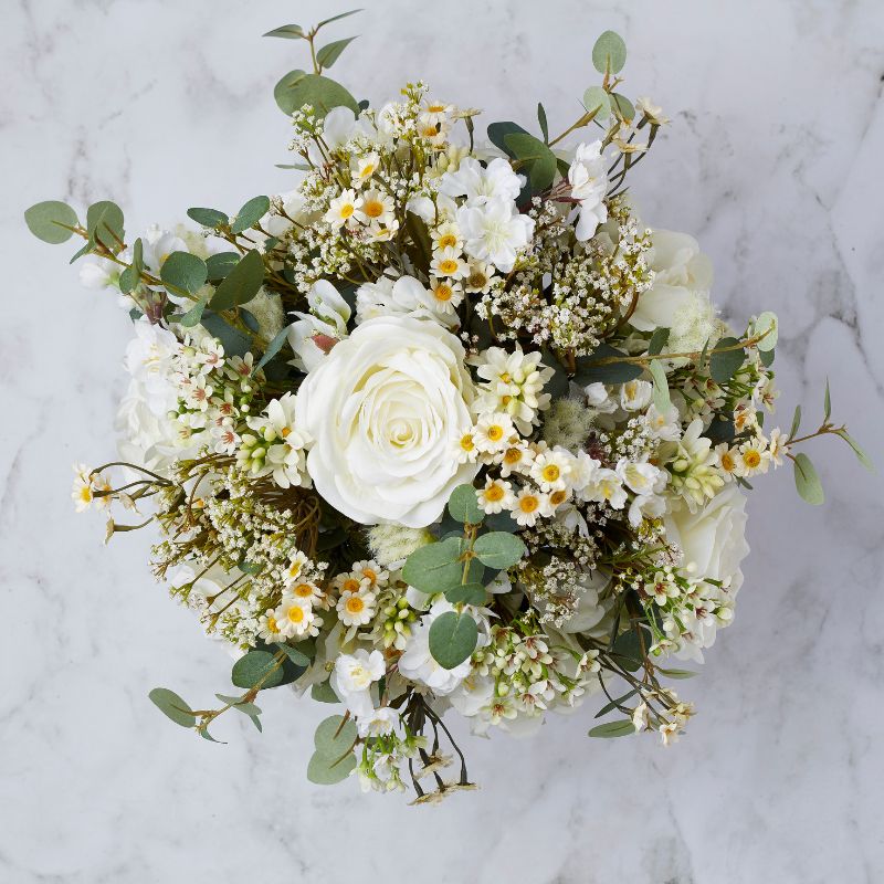 Top view of an ivory-themed artificial floral bouquet with white roses, delicate daisies, and lush greenery.